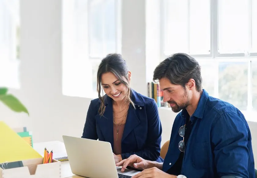 Dos personas de un equipo trabajando juntas frente a un computador portátil en una oficina con luz natural